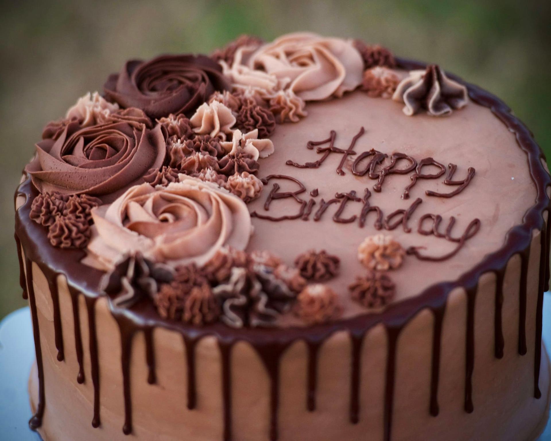 A chocolate drip cake topped with buttercream roses and a birthday message