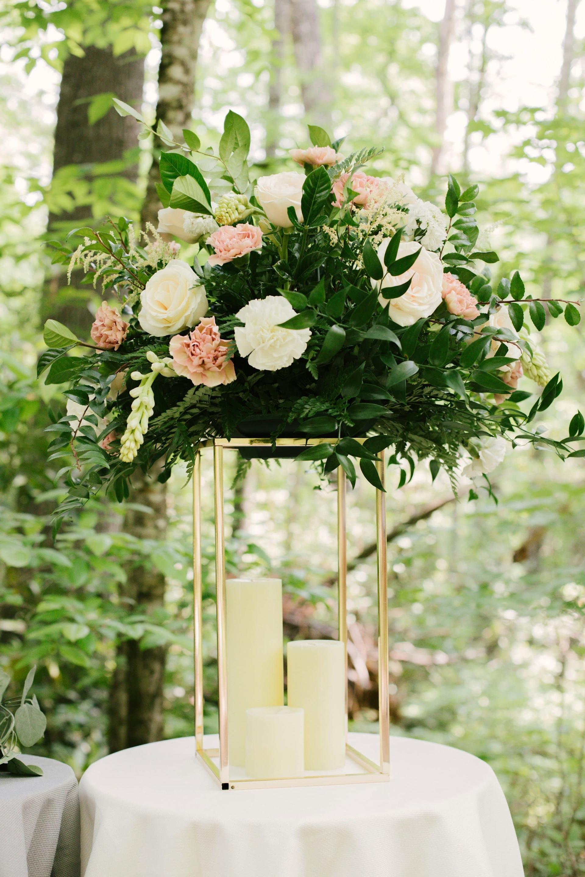 A tall floral arrangement on a gold stand with pillar candles