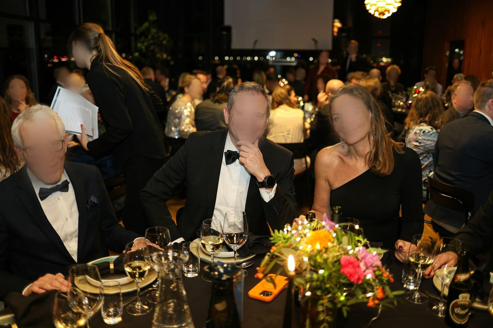 Three guests in formal evening wear at a gala dinner table