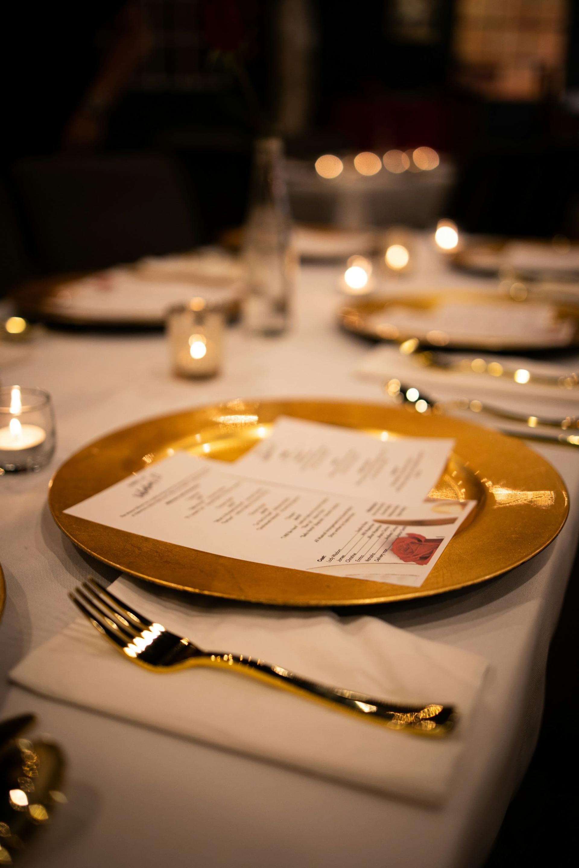 A gold charger plate holding a printed menu at a formal dinner place setting