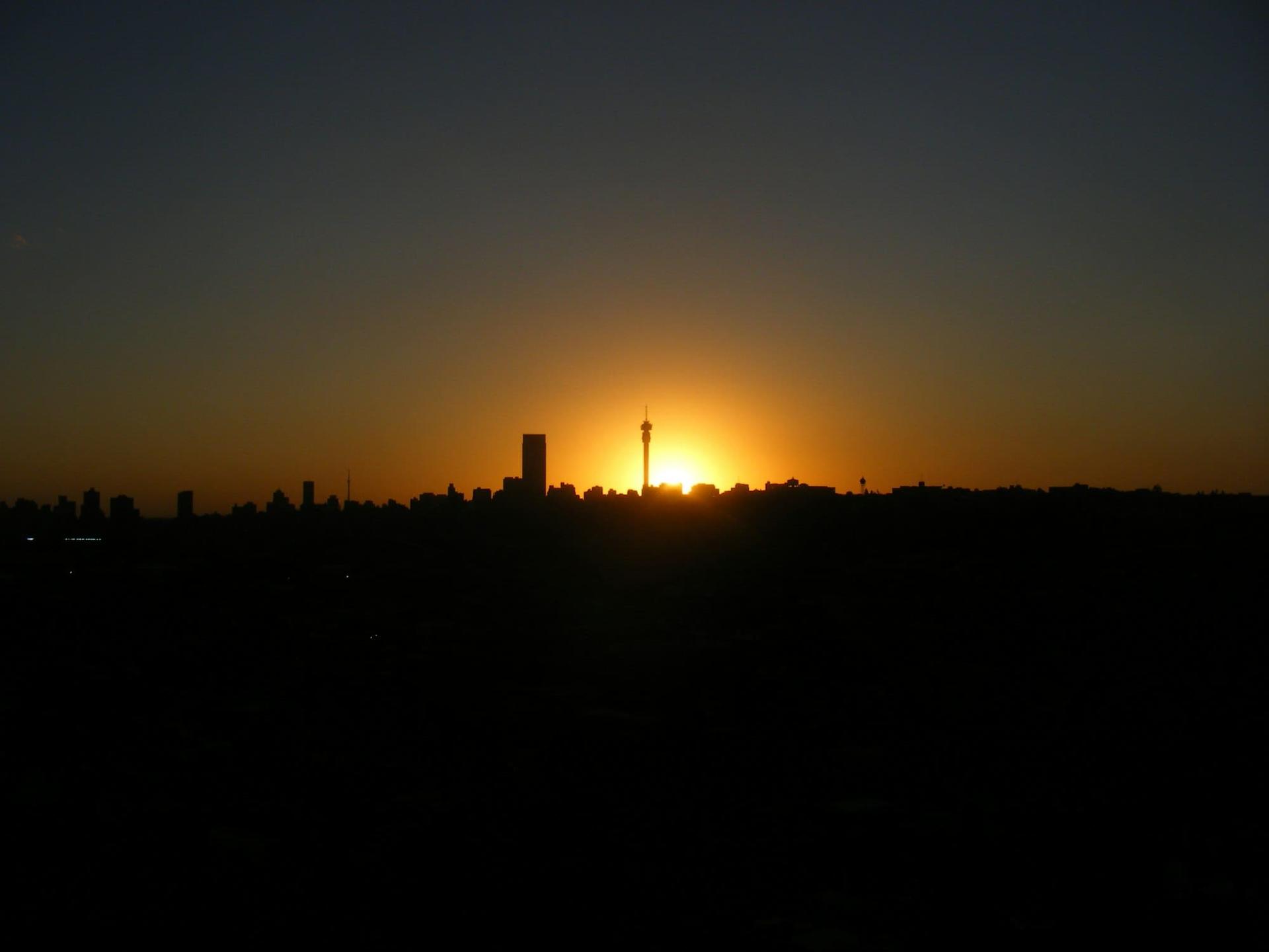 A city skyline and its tall communications tower in silhouette as the sun sets behind them