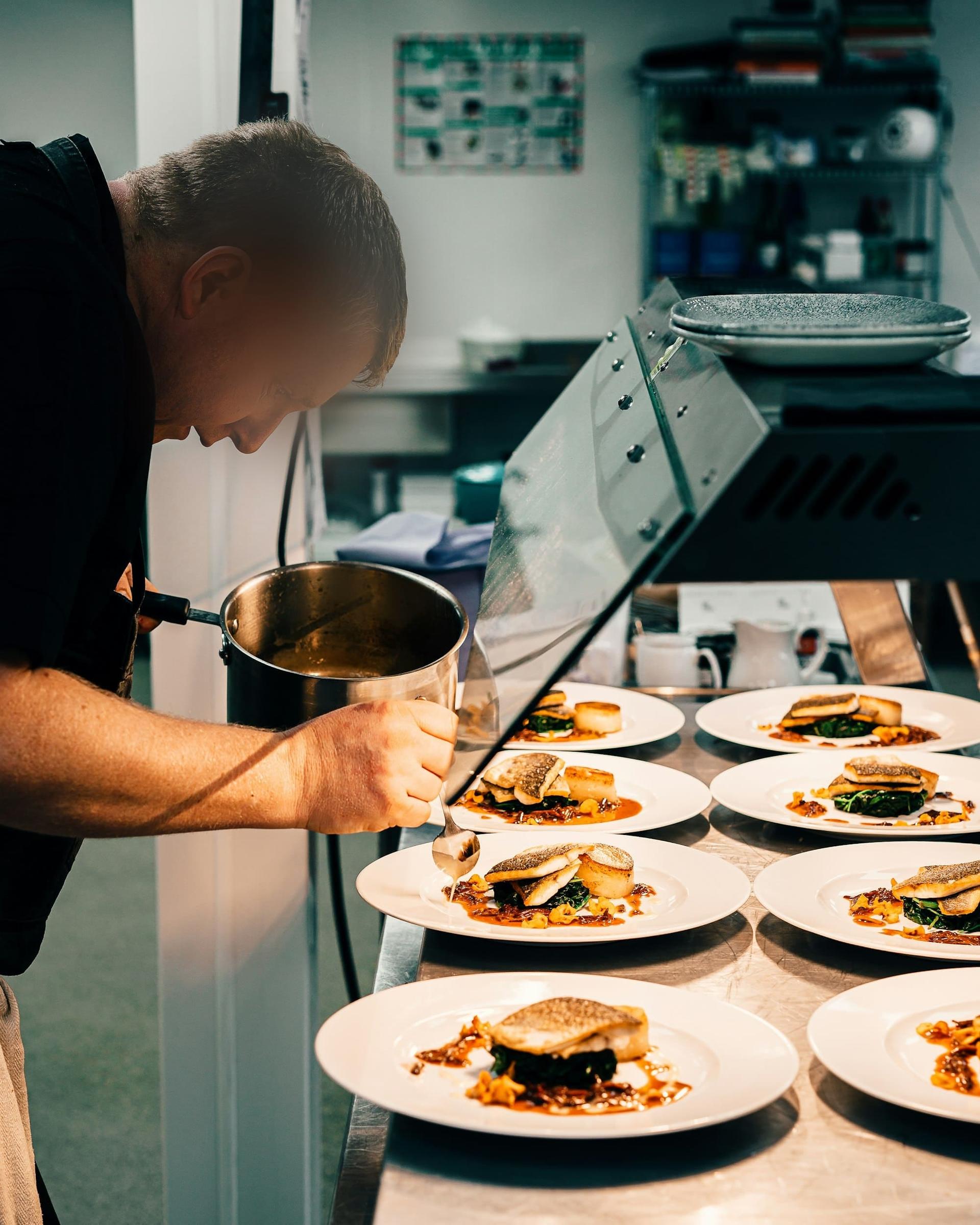 A chef saucing a line of plated mains before service