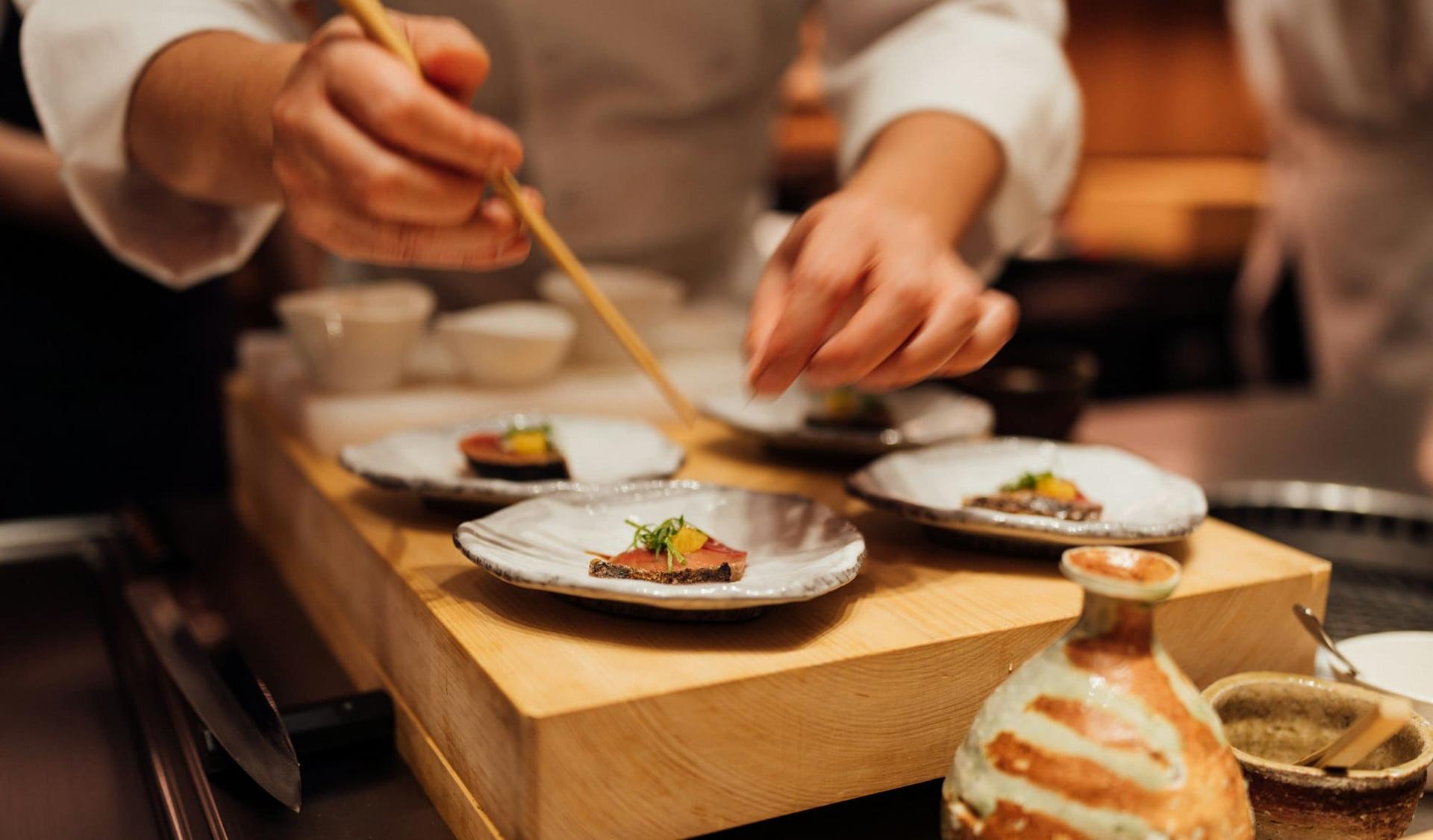 Chefs plating small courses together on a wooden board