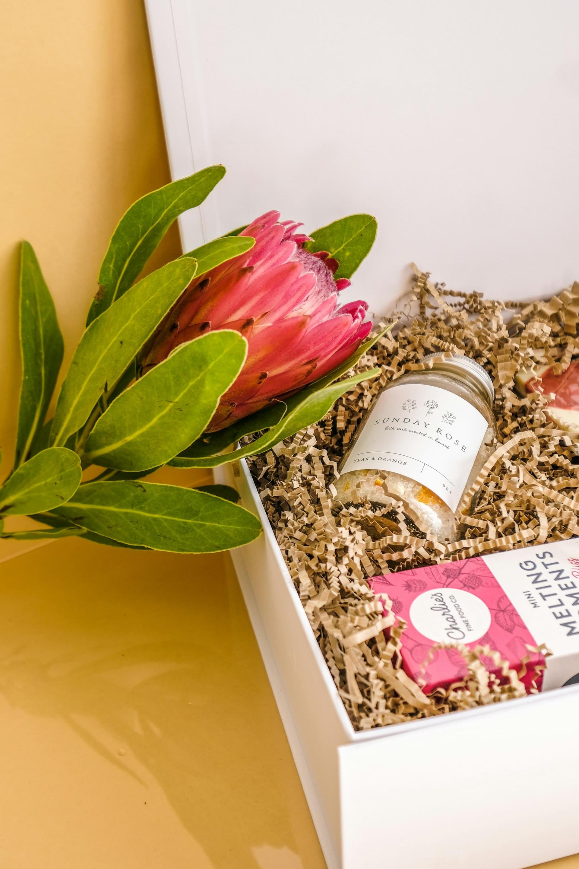 A gift box with a protea, a candle and wrapped treats in shredded paper