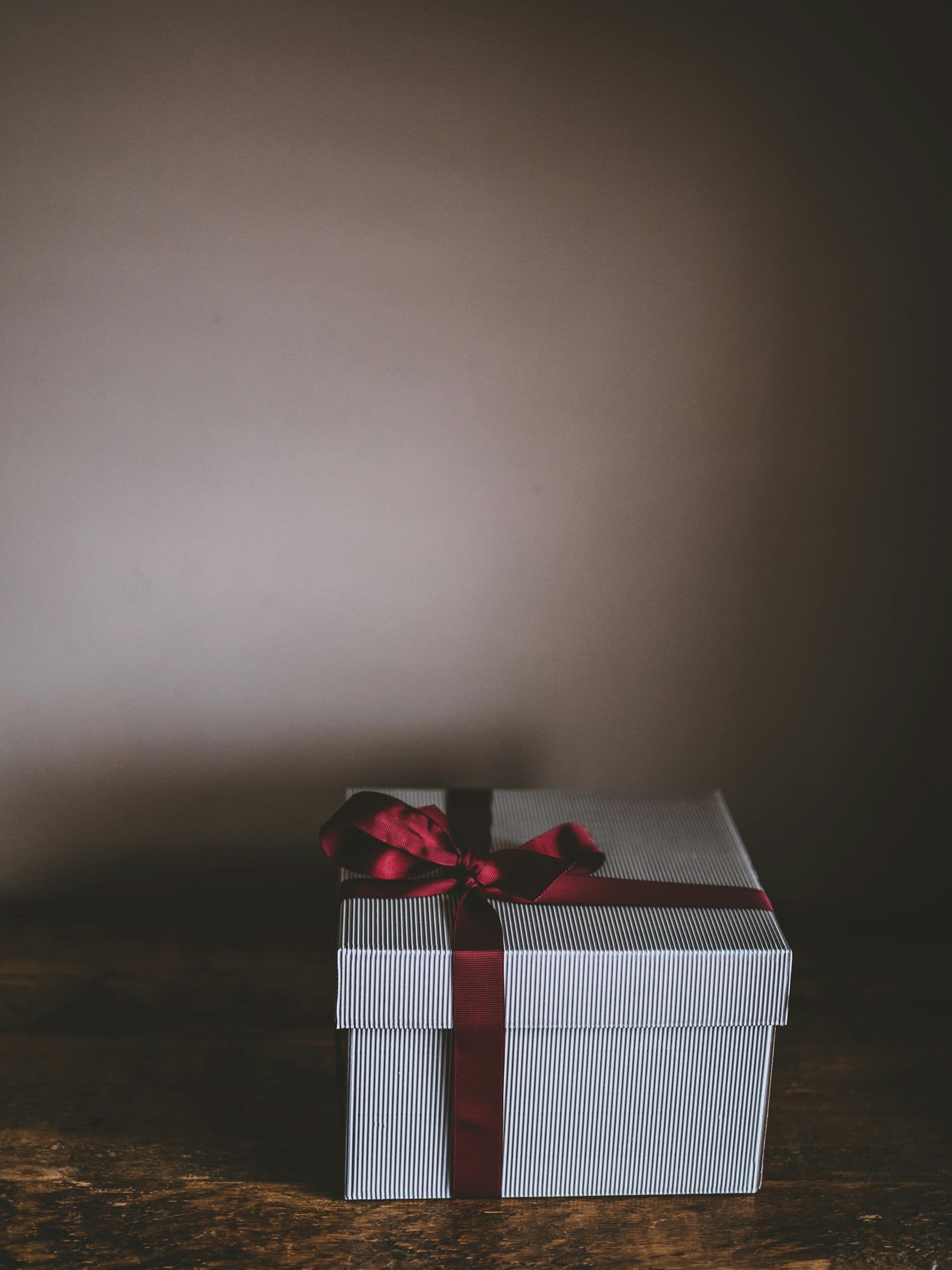 A white gift box tied with a deep red ribbon against a dark backdrop
