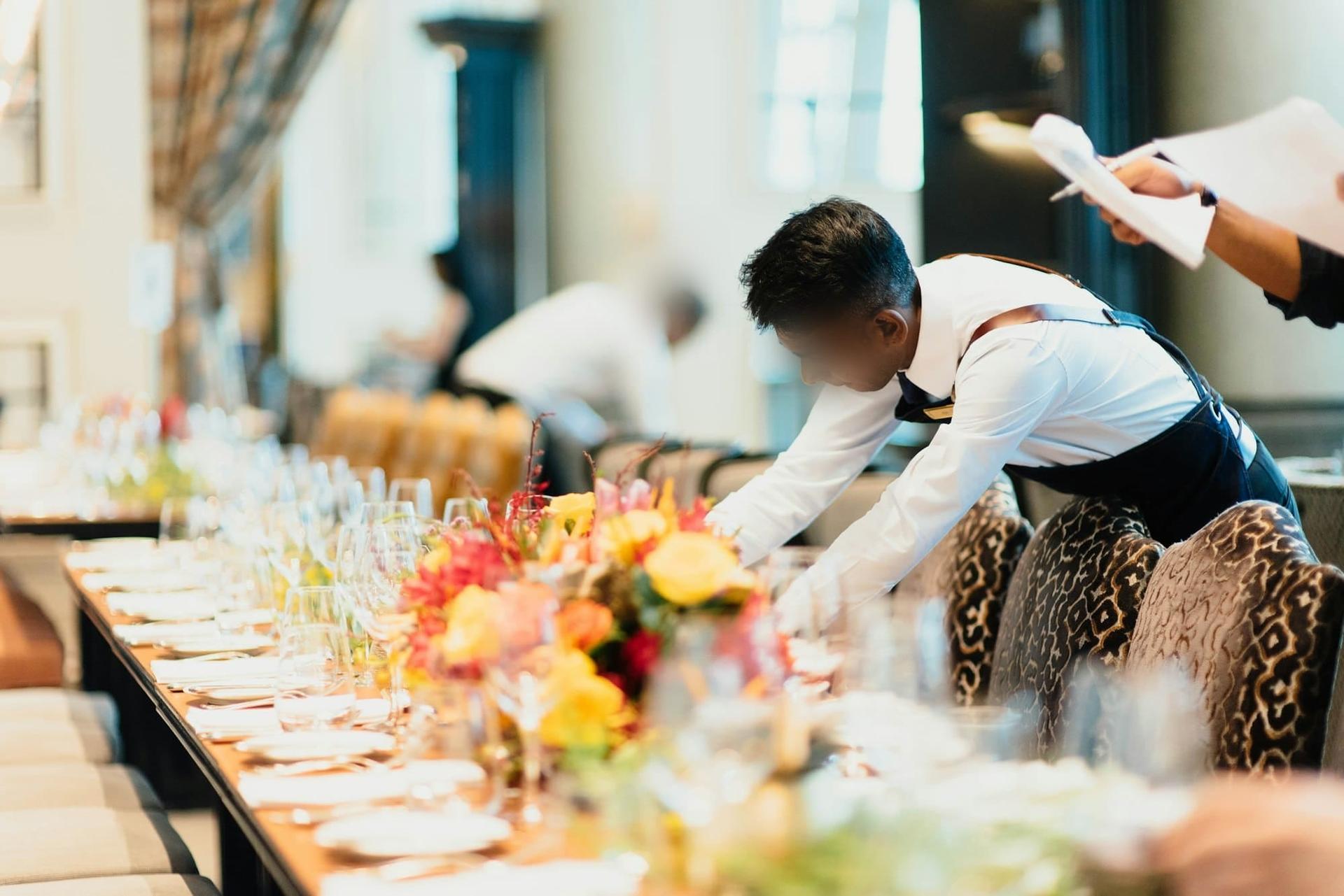 Hospitality staff setting a long table with flowers and glassware