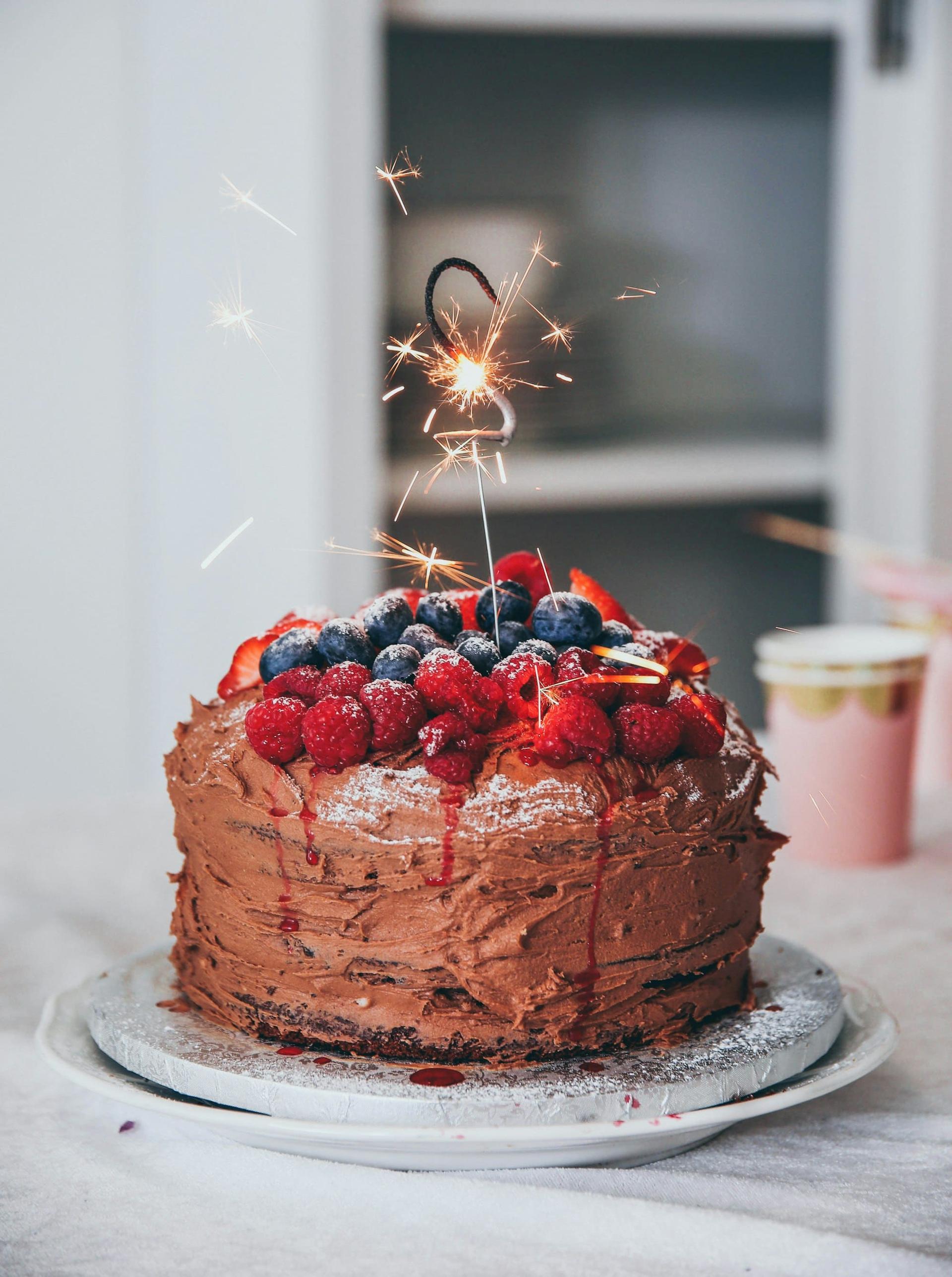 A berry-topped chocolate cake with a lit sparkler