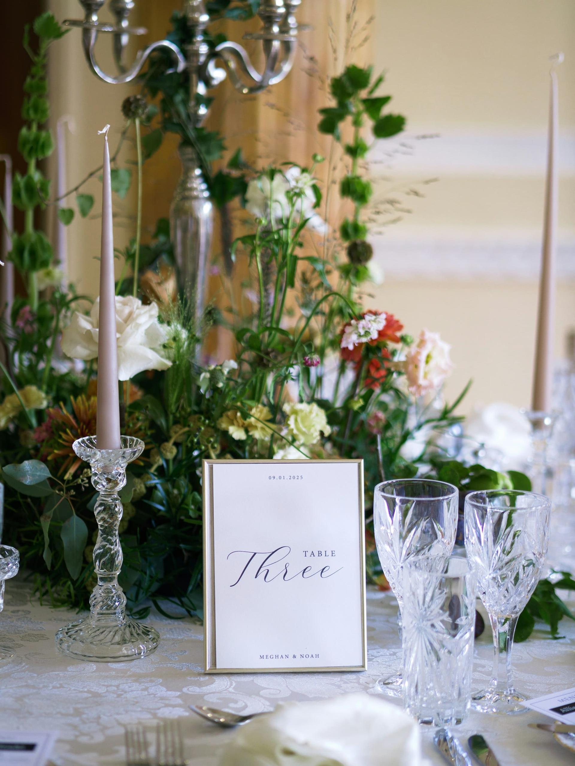 A floral centrepiece with taper candles and a table number card