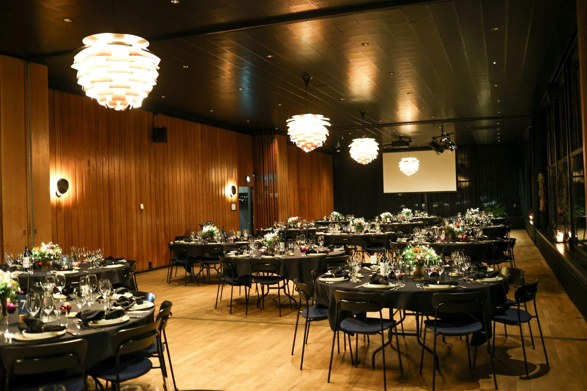 A wood-panelled function room set with dark round tables for dinner