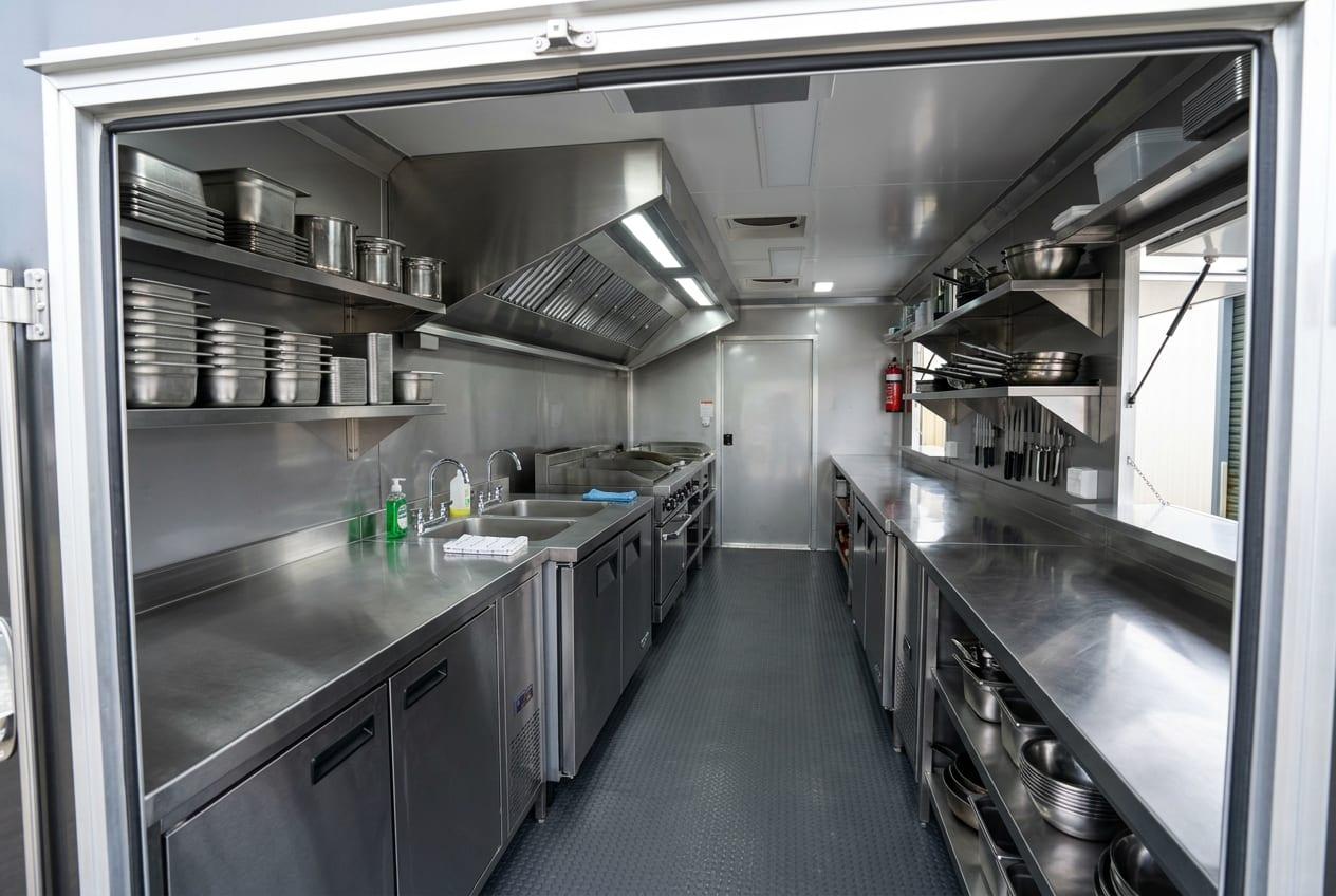 Inside a mobile kitchen trailer with stainless steel prep counters, shelving and an extraction canopy