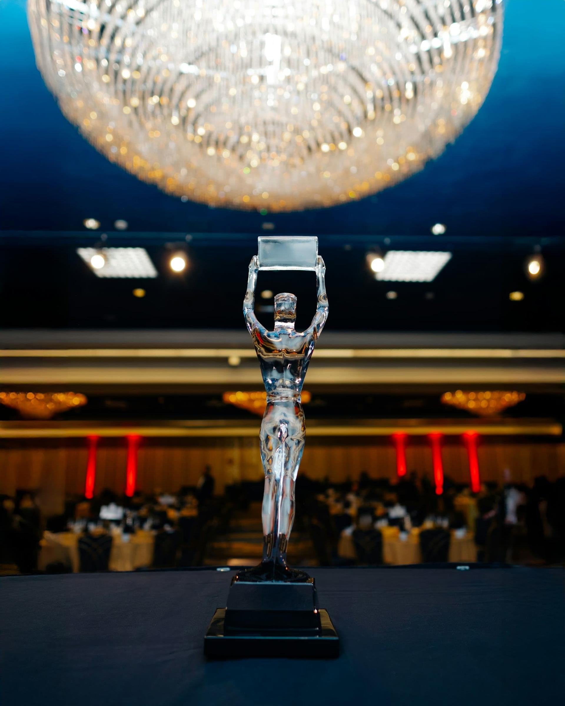 An award trophy on stage in front of a ballroom set for an awards dinner