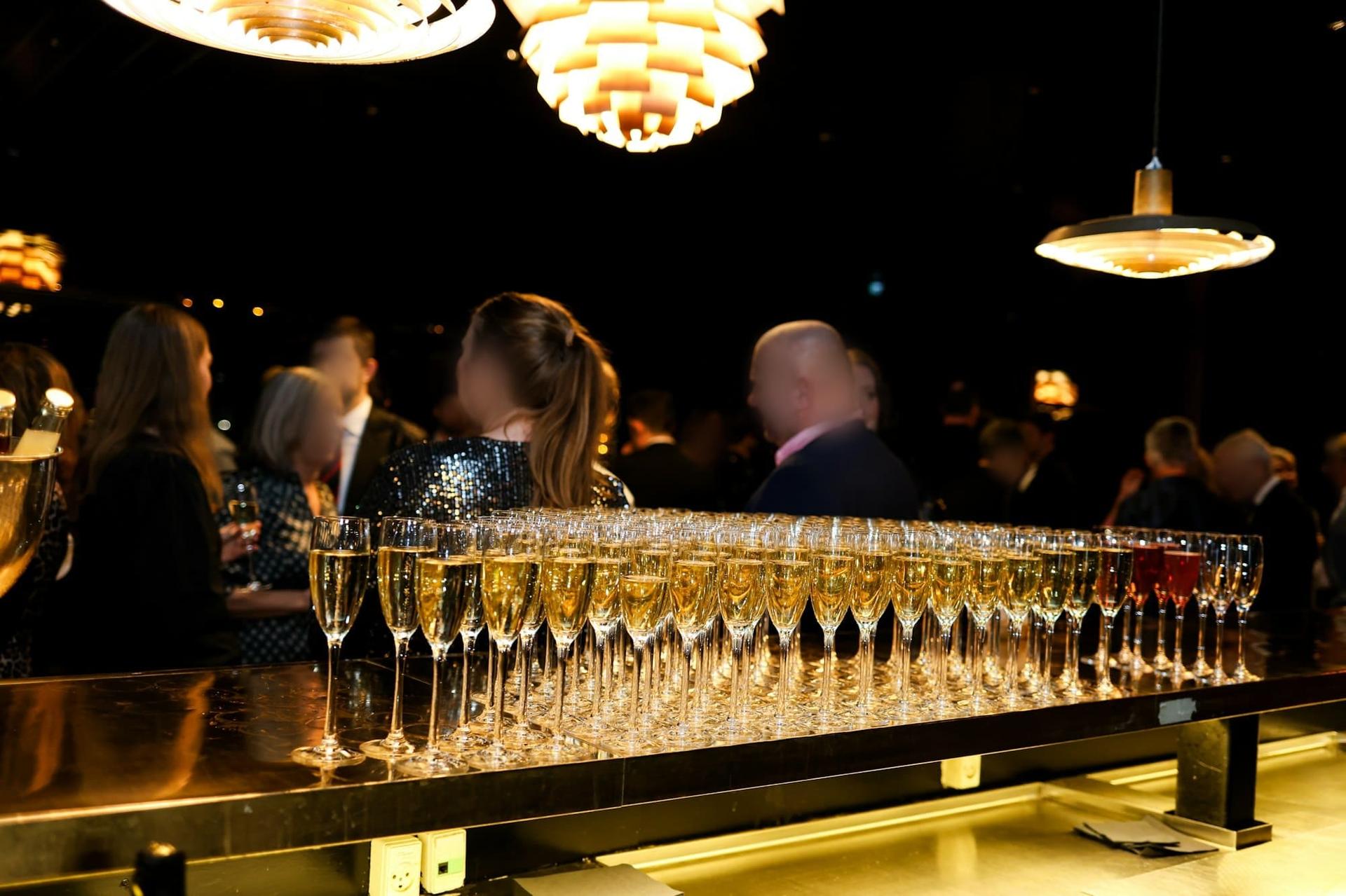 Rows of champagne flutes on a bar as guests mingle at an evening reception