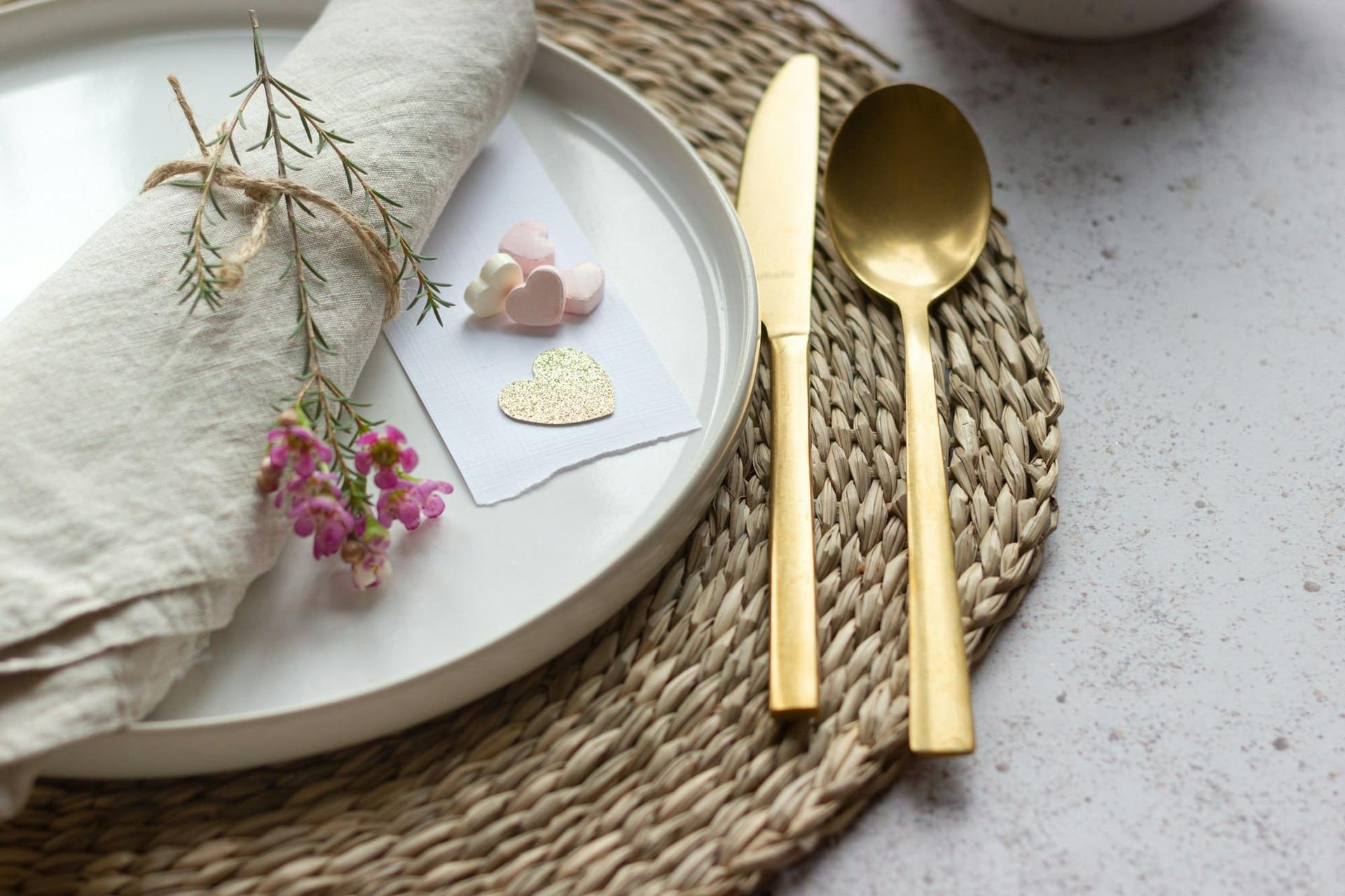 A rattan charger with a white plate, linen napkin and gold cutlery